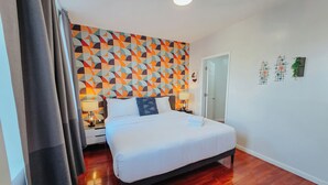 A hotel room with a bed, wooden flooring, a geometric patterned wall, and a door. - Vale / King Bed / Elevator / Balcony / Ensuite (Philadelphia)