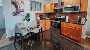 A modern kitchen with wooden cabinets, a stainless steel microwave, an oven, and a dining area with a glass table and chairs. - Vale / King Bed / Elevator / Balcony / Ensuite (Philadelphia)