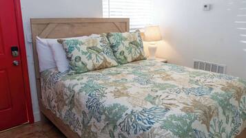 Une chambre à coucher avec une tête de lit en bois, un lit recouvert d’une couvre-lit à motifs floraux, des oreillers blancs, une lampe de chevet et une porte rouge.