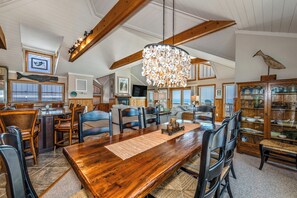 A spacious dining area with a wooden table and chairs, a chandelier, and a view of the kitchen and living area. - Oceanfront, elevator, pool, hot tub, walk to shops. Friday check in. (Kitty Hawk)