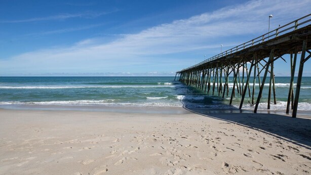 A beach with a wooden pier extending into the ocean. - Doc's Beachy Boardwalk (Kure Beach)