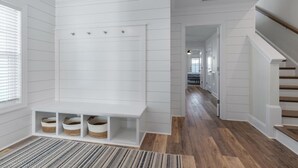 A modern, clean hallway with a built-in bench and baskets, wooden flooring, and a staircase. - Doc's Beachy Boardwalk (Kure Beach)