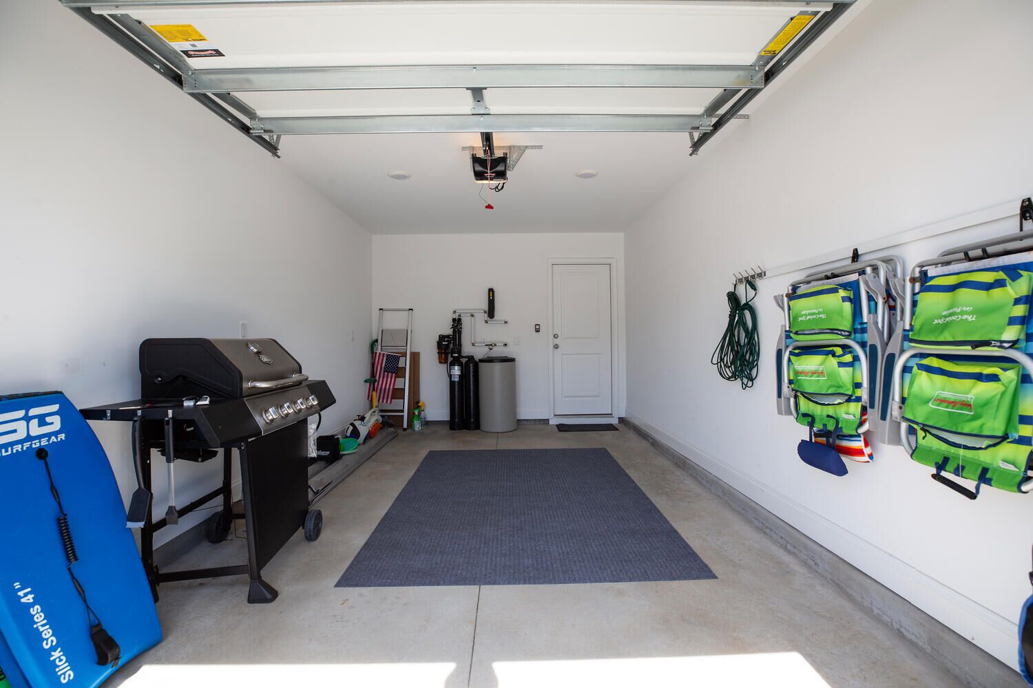 A garage with a barbecue grill, a ladder, a trash can, and a door.