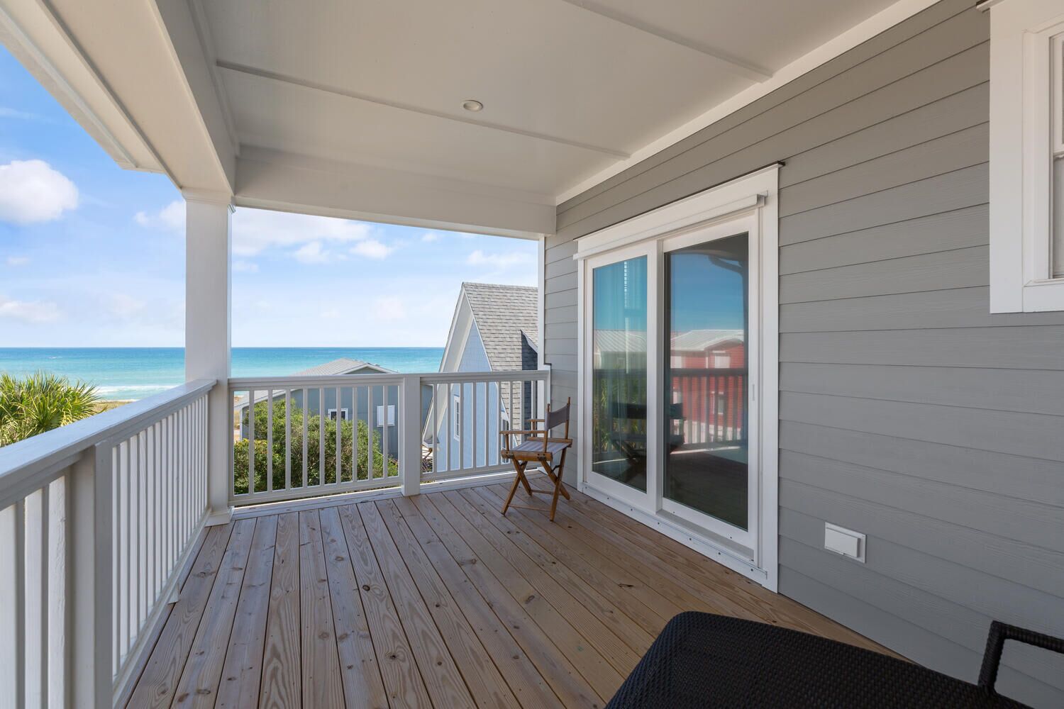 A wooden deck with a view of the ocean, a sliding glass door, and a chair.