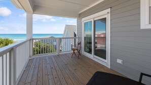 A wooden deck with a view of the ocean, a sliding glass door, and a chair. - Doc's Beachy Boardwalk (Kure Beach)