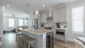A modern kitchen with a large island, stainless steel appliances, and pendant lighting. - Doc's Beachy Boardwalk (Kure Beach)
