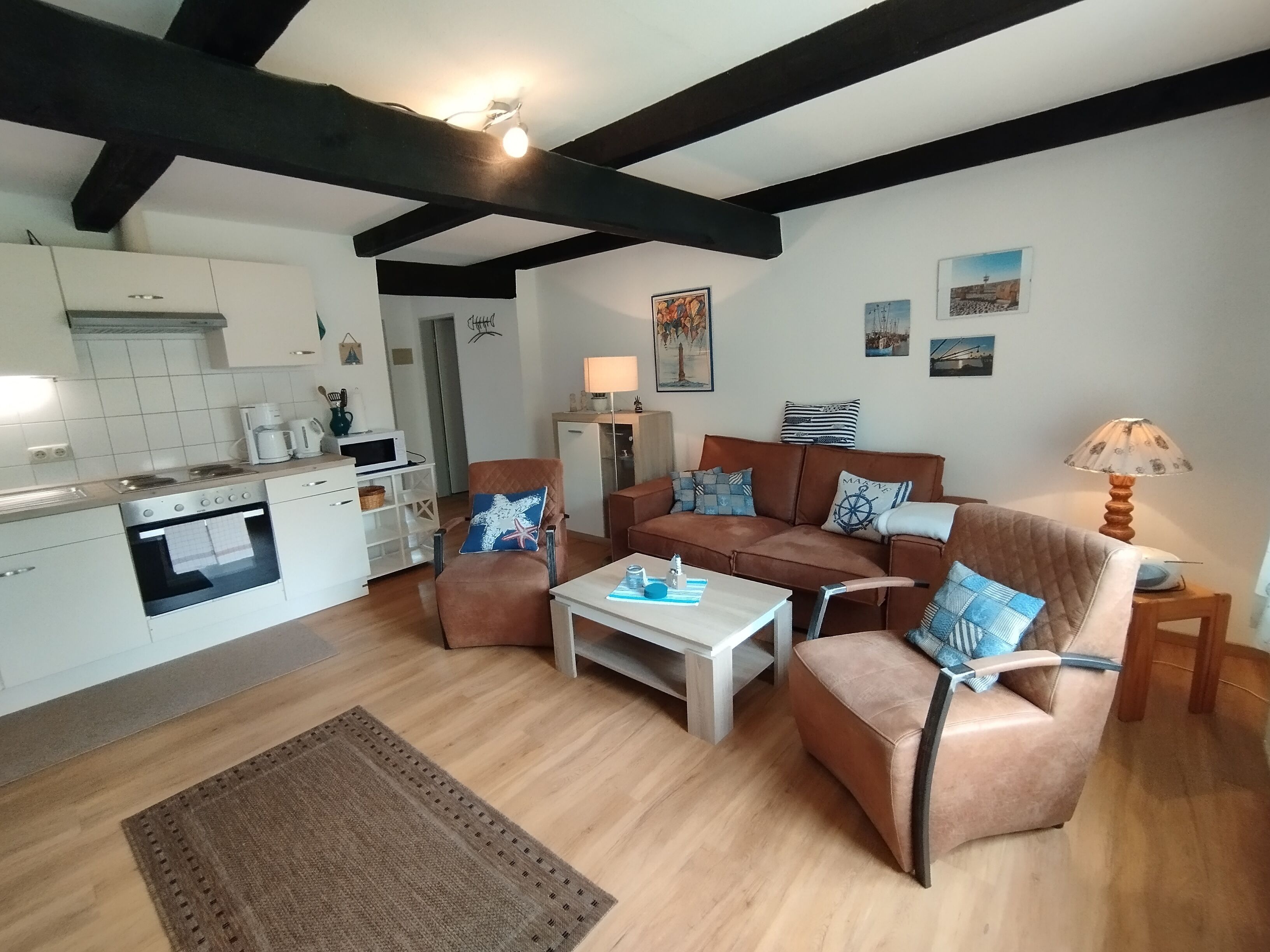 A modern kitchen with white cabinets and a built-in oven, a brown leather sofa set with blue cushions, a wooden coffee table, and a small rug on the floor.