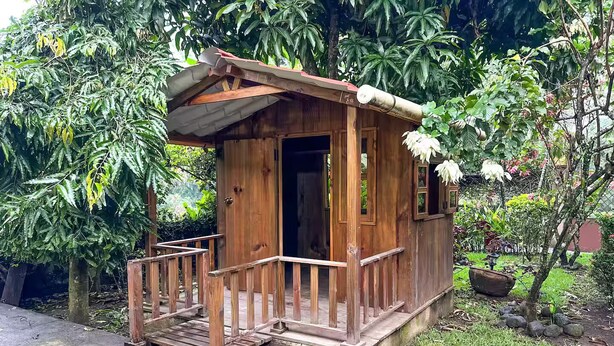 A small wooden structure with a porch, surrounded by lush greenery. - Casa cómoda y tranquila a minutos de Xetulul (Guatemala)