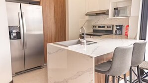 A modern kitchen with a marble island, stainless steel appliances, and grey bar stools. - Cómodo apartamento a minutos de cayala (Guatemala City)