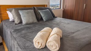 A neatly made bed with a grey textured bedspread, two pillows, and two rolled towels. - Cómodo apartamento a minutos de cayala (Guatemala City)
