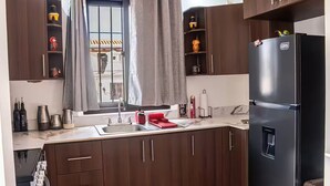 Eine moderne Küche mit dunklen Holdekor-Schränken, einem schwarzen Kühlschrank und einem Fenster mit grauen Vorhängen.