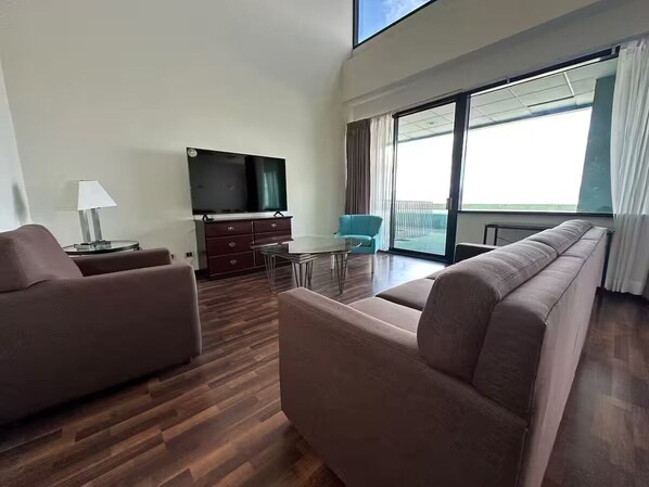 Ein modernes Wohnzimmer mit einer Couch, einem Fernseher, einem kleinen Tisch und Meerblick durch große Fenster.