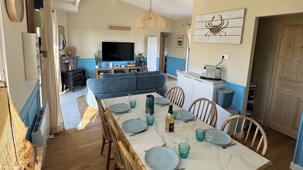 A dining area with a marble table set for six, wooden chairs, and a kitchen in the background. - Villa les dunes (Merlimont)