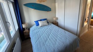 A bedroom with a bed, a surfboard decoration, a window with curtains, and a wooden floor. - Villa les dunes (Merlimont)
