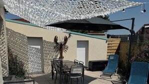 A patio area with a table and chairs, a large umbrella, and a decorative white canopy. - Villa les dunes (Merlimont)