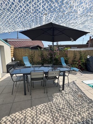 An outdoor patio with a glass table and chairs, a large umbrella, and a decorative ceiling. - Villa les dunes (Merlimont)