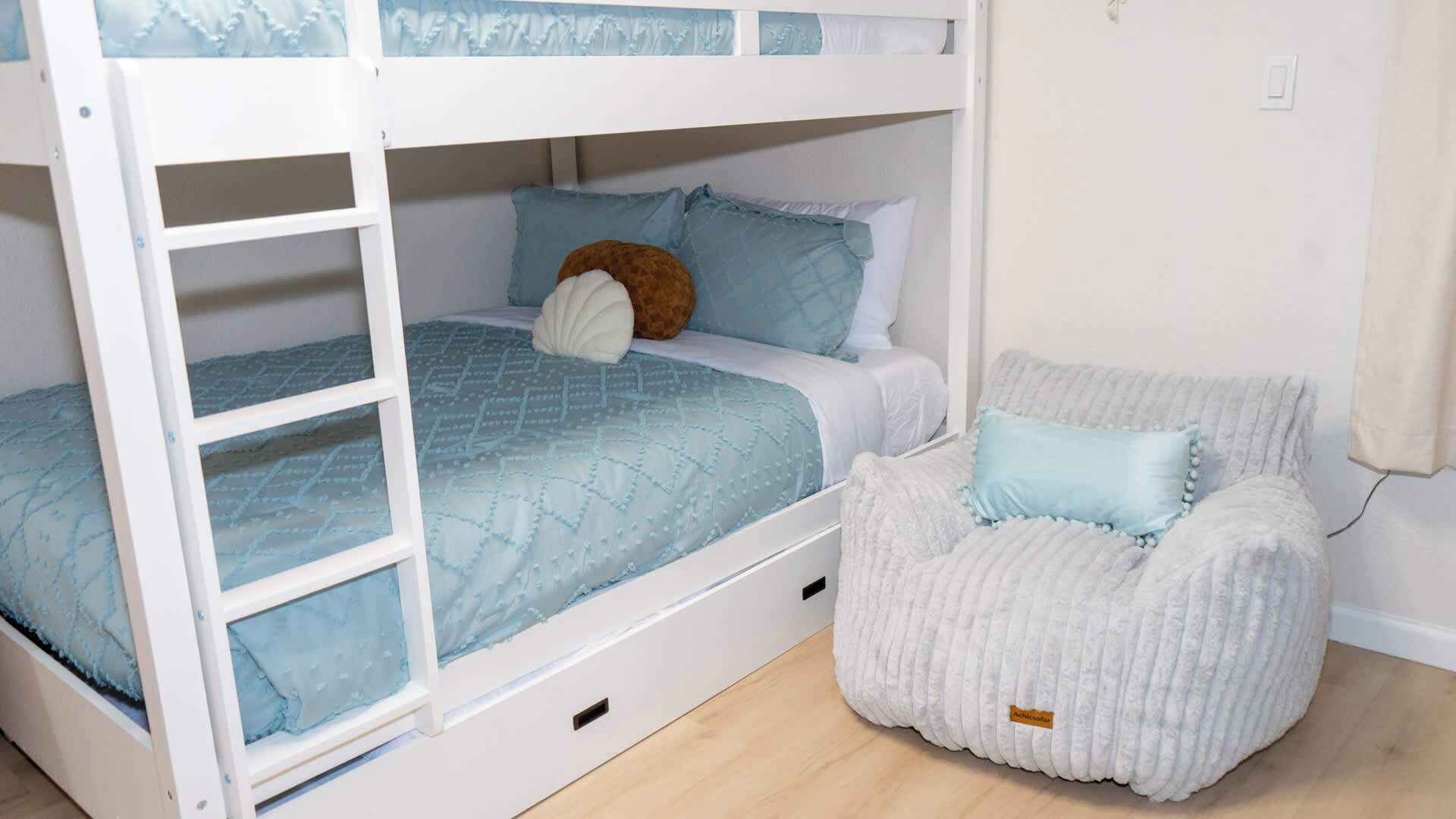 Un letto a castello con una coperta blu, un orsetto di peluche e una sedia bianca con un'etichetta.