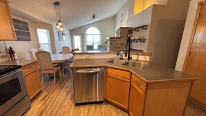 A modern kitchen with wooden cabinets, a stainless steel dishwasher, and a large island with a sink. - Calgary Home | 3BR Home | Sleeps 6 | Parking | 15min to Downtown (Calgary)