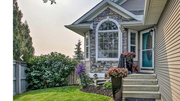 A two-story house with a stone facade, a front porch with steps, and a small garden with flowers. - Calgary Home | 3BR Home | Sleeps 6 | Parking | 15min to Downtown (Calgary)