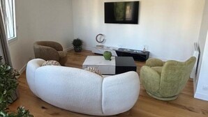 A modern living room with a white sofa, a green armchair, a coffee table, a flat-screen TV, and a small plant.