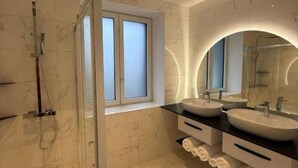 A modern bathroom with two sinks, a shower, and a window.