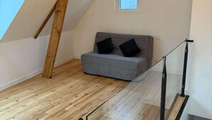 A room with a sloped ceiling, a grey sofa with black cushions, and a wooden floor.