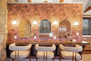 A vanity with three mirrors, a window, and a wall with a floral pattern.