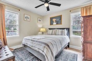 A bedroom with a bed, a ceiling fan, a lamp, a window with curtains, and a cabinet.