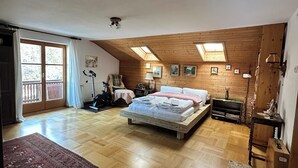 Tilava makuuhuone, jossa on puinen katto, suuri sänky, kattovalokuvio ja näkymä ulos.