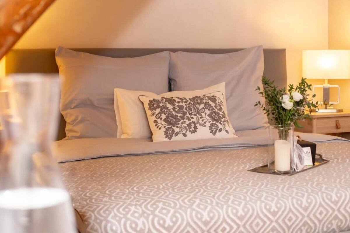 A neatly made bed with a patterned bedspread, a decorative pillow, and a bedside table with a lamp and a vase of flowers.