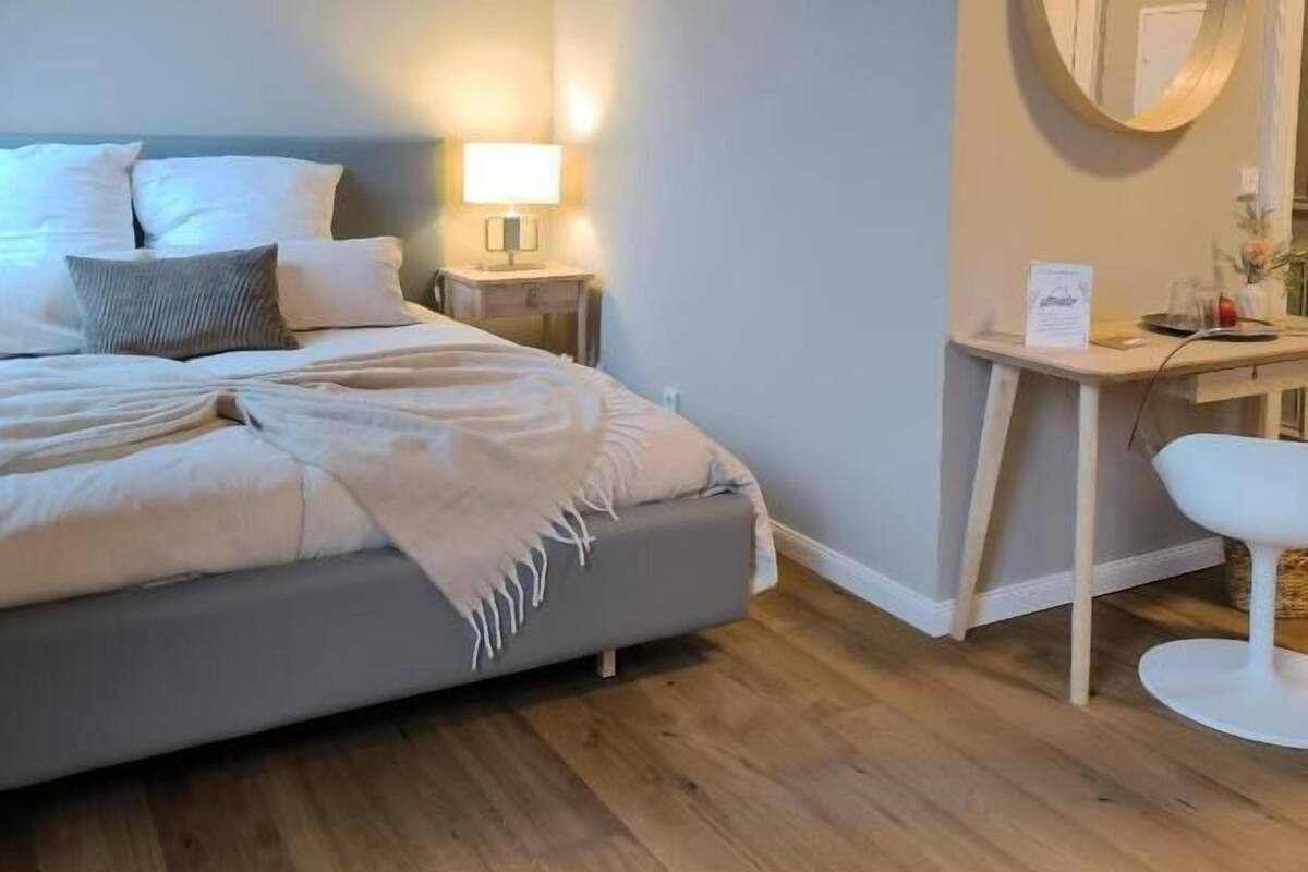A bedroom with a bed, bedside table, lamp, and a desk with a chair.