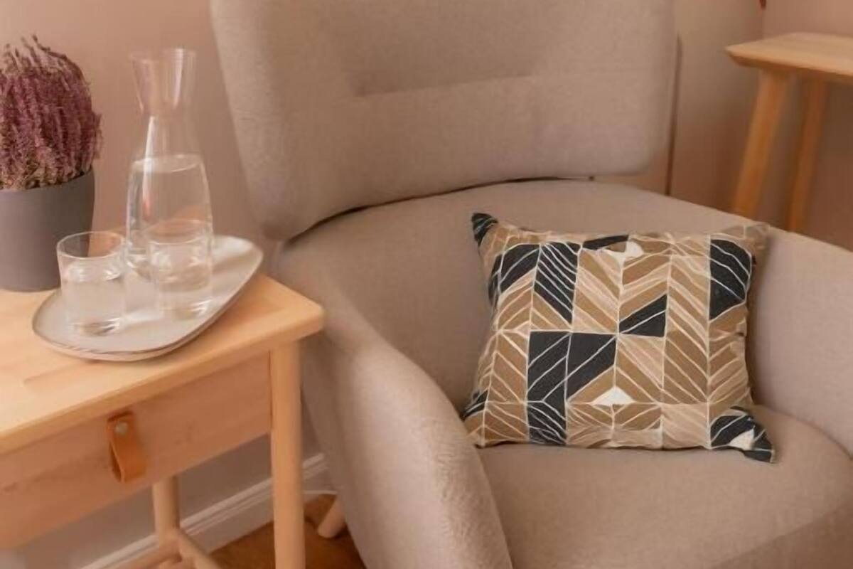 A cozy seating area with a cushioned chair, a small table with a lamp, and a decorative pillow.