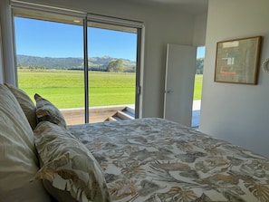A bedroom with a bed, a large window, and a door leading outside. - Runway Retreat Enchanting Whitianga 3-bedroom House (Whitianga)