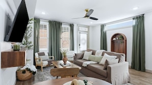 Uma sala de estar moderna com sofá, poltronas, mesa de centro, televisão e ventilador de teto.