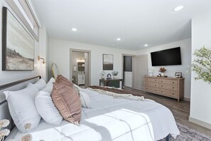 A bedroom with a bed, bedside table, dresser, and a TV mounted on the wall.