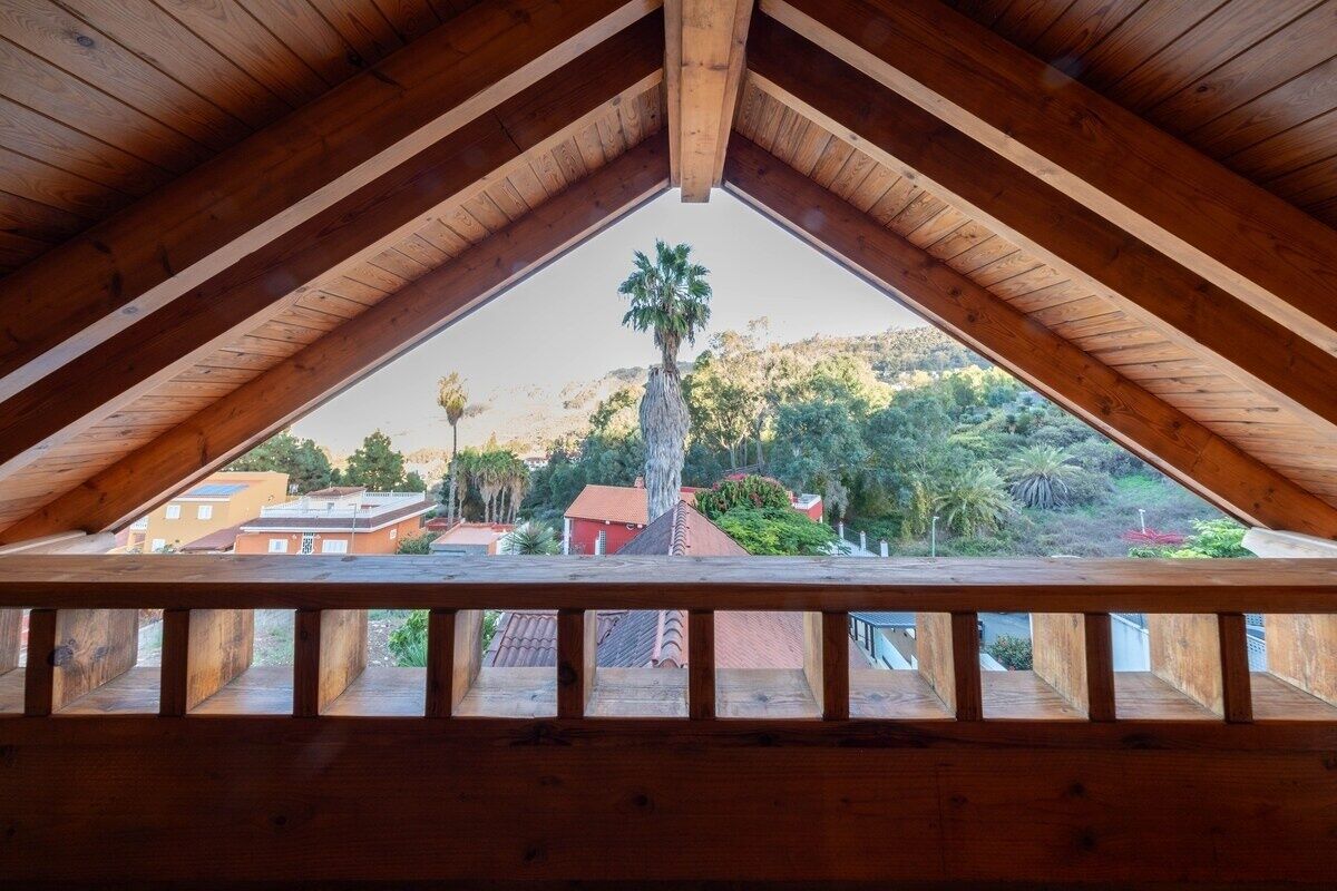 Un balcon en bois offrant une vue sur un palmier et les bâtiments environnants.
