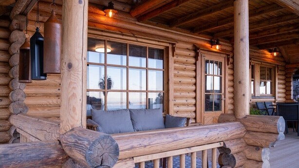 A log cabin with a wooden bench and a table, large windows, and a stone fireplace. - Cabin Tranquil Organic Heated Pool (La Solana)