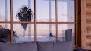 A room with a large window reflecting a palm tree and a mountainous landscape. - Cabin Tranquil Organic Heated Pool (La Solana)