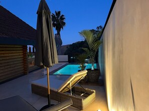 Un patio trasero con piscina, sillas de descanso y un pérgola.