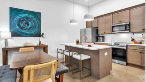 A modern kitchen with wooden cabinets, a central island, stainless steel appliances, and a dining area with a table and chairs. - Three bedroom  in United States of America, Spartanburg (Spartanburg)
