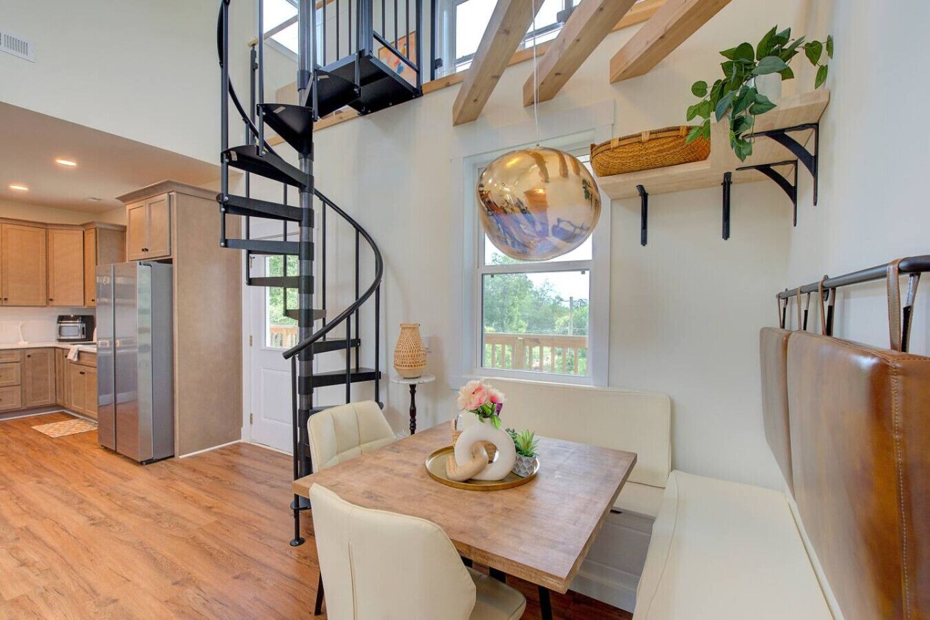 A modern kitchen with a spiral staircase, wooden flooring, and a dining area with a table set for two.