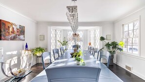 Un espace repas avec une longue table, des chaises, des plantes en pot et un lustre.