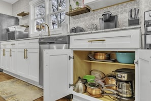 A kitchen with white cabinets, a dishwasher, and various cooking utensils.