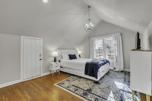A bedroom with a bed, bedside tables, a chandelier, a window with curtains, and a white wardrobe.