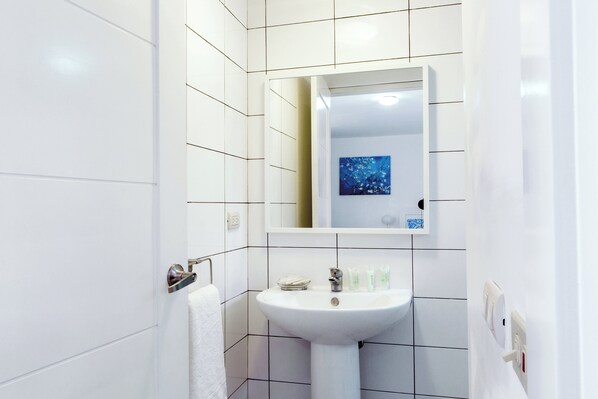 A bathroom with white tiles, a sink, a mirror, and a towel rack. - BRISAS TROPICAL playa LOS CORALES (Punta Cana)