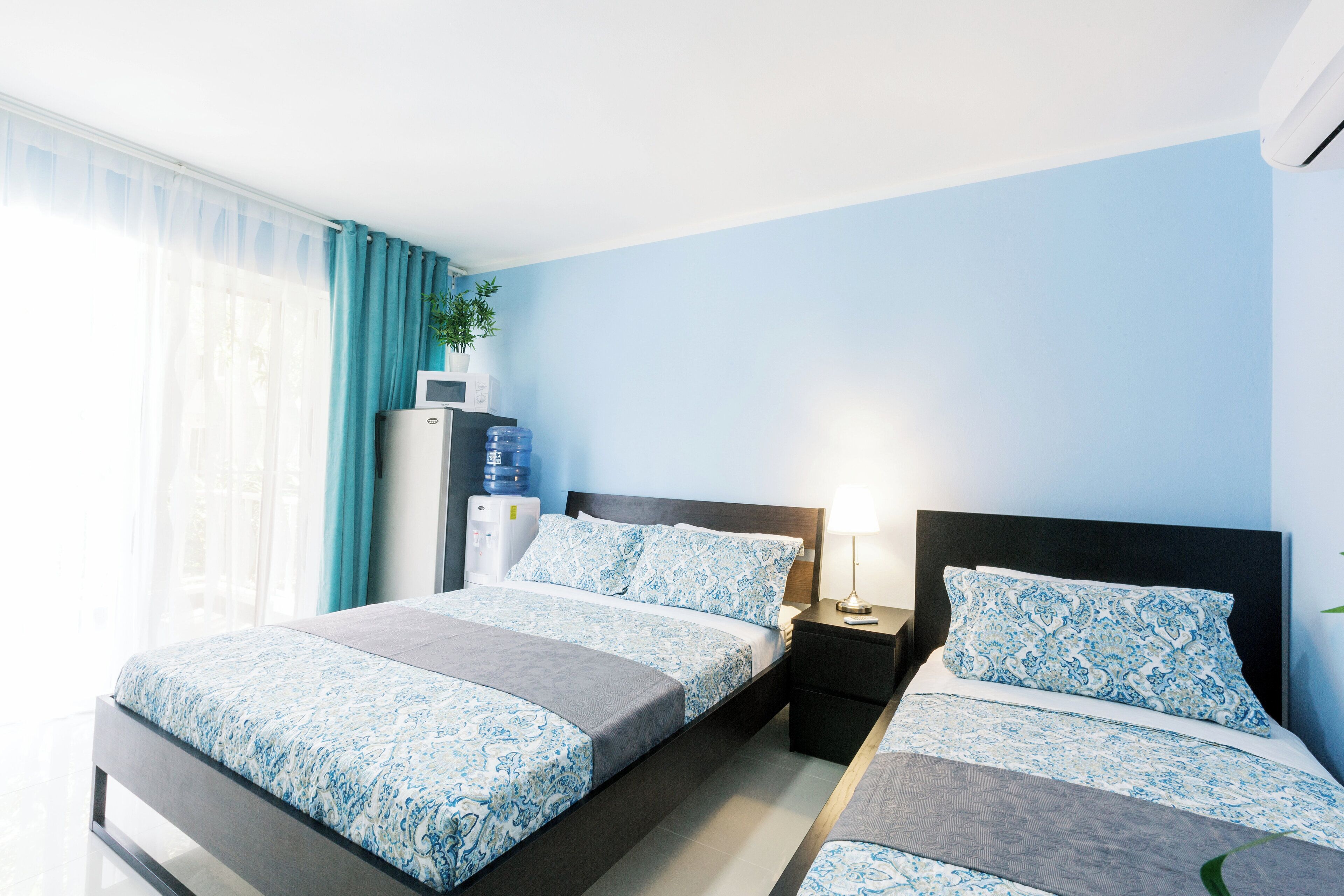 A hotel room with two beds, a desk, a water dispenser, and a plant.