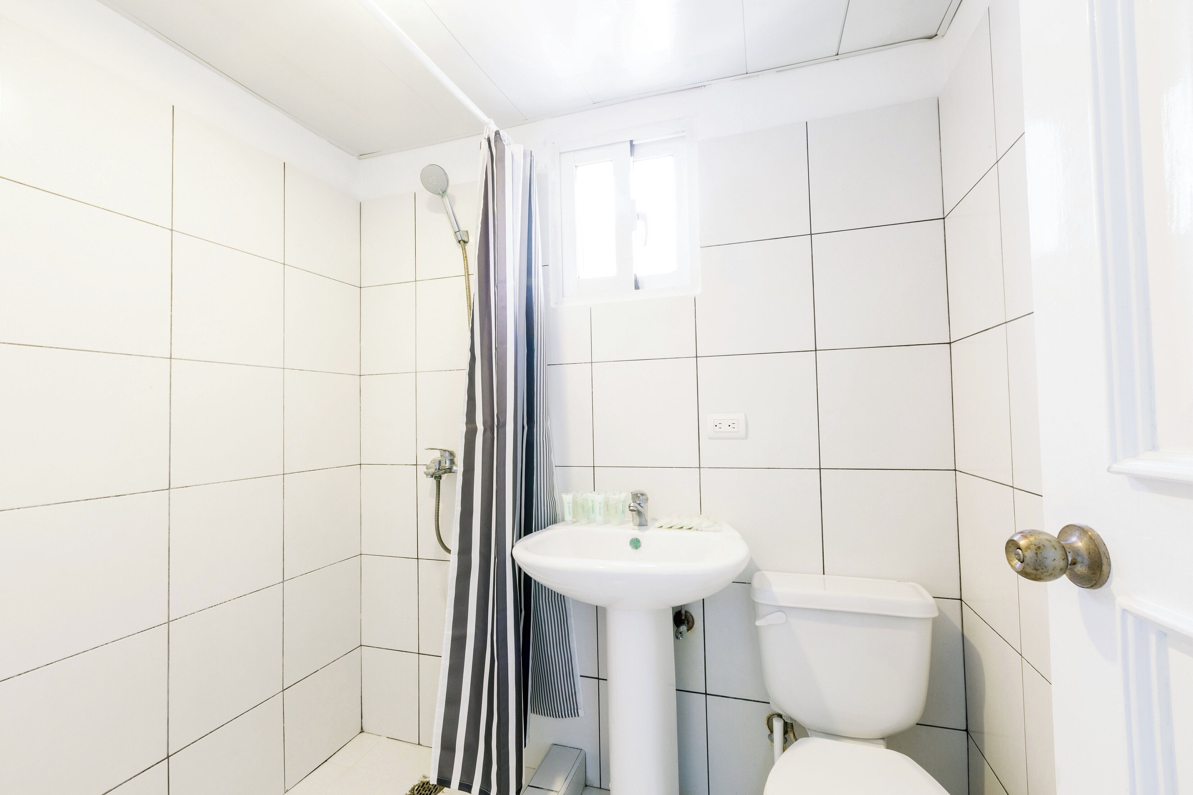 A bathroom with white tiled walls, a white sink, a toilet, and a shower with a striped curtain.