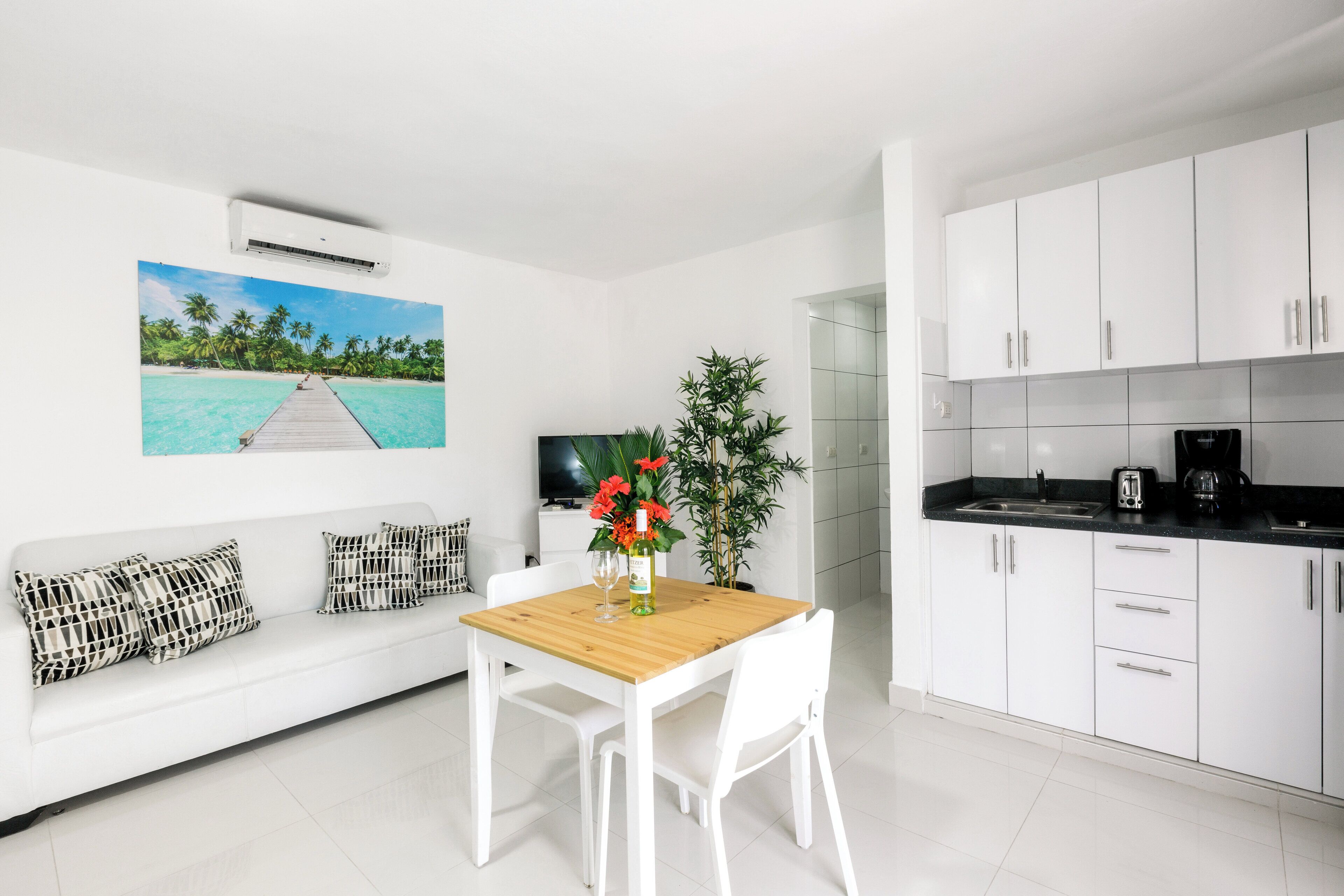 A modern kitchen with white cabinets, a wooden dining table, and a white sofa.