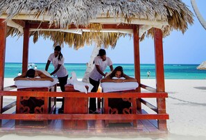 Een massagesalon aan het strand, met houten banken en rieten daken.