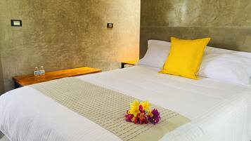 A hotel room with a large bed, a wooden nightstand, a water bottle, and a flower arrangement.